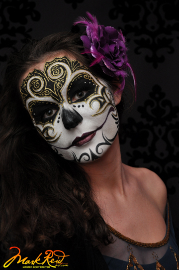 woman in full face paint with a skull feel in white black and gold